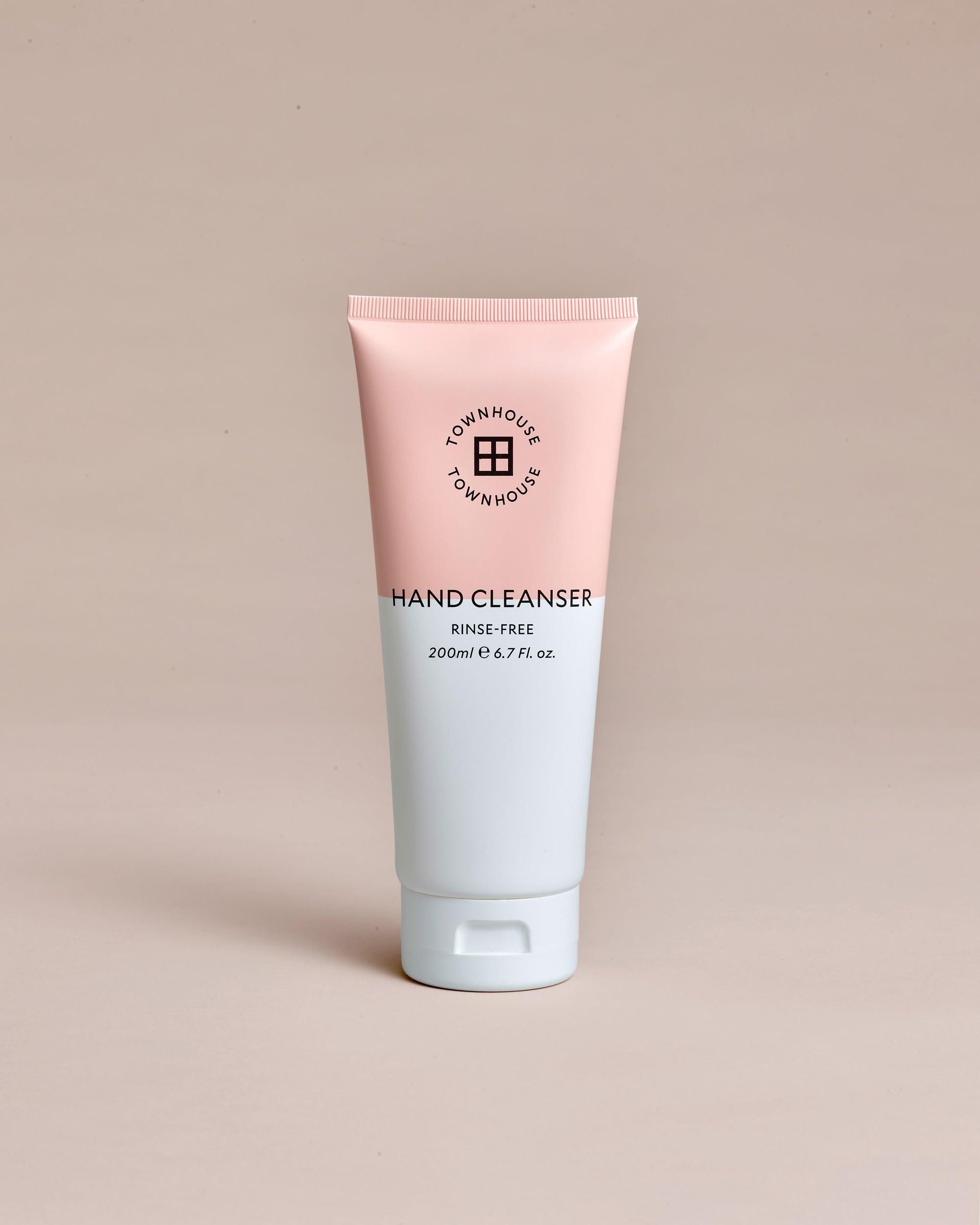 A pink and white tube labeled Townhouse Hand Cleanser 200ml stands upright on a plain beige background, emphasizing its gentle, effective rinse-free formula for hand cleansing without water.