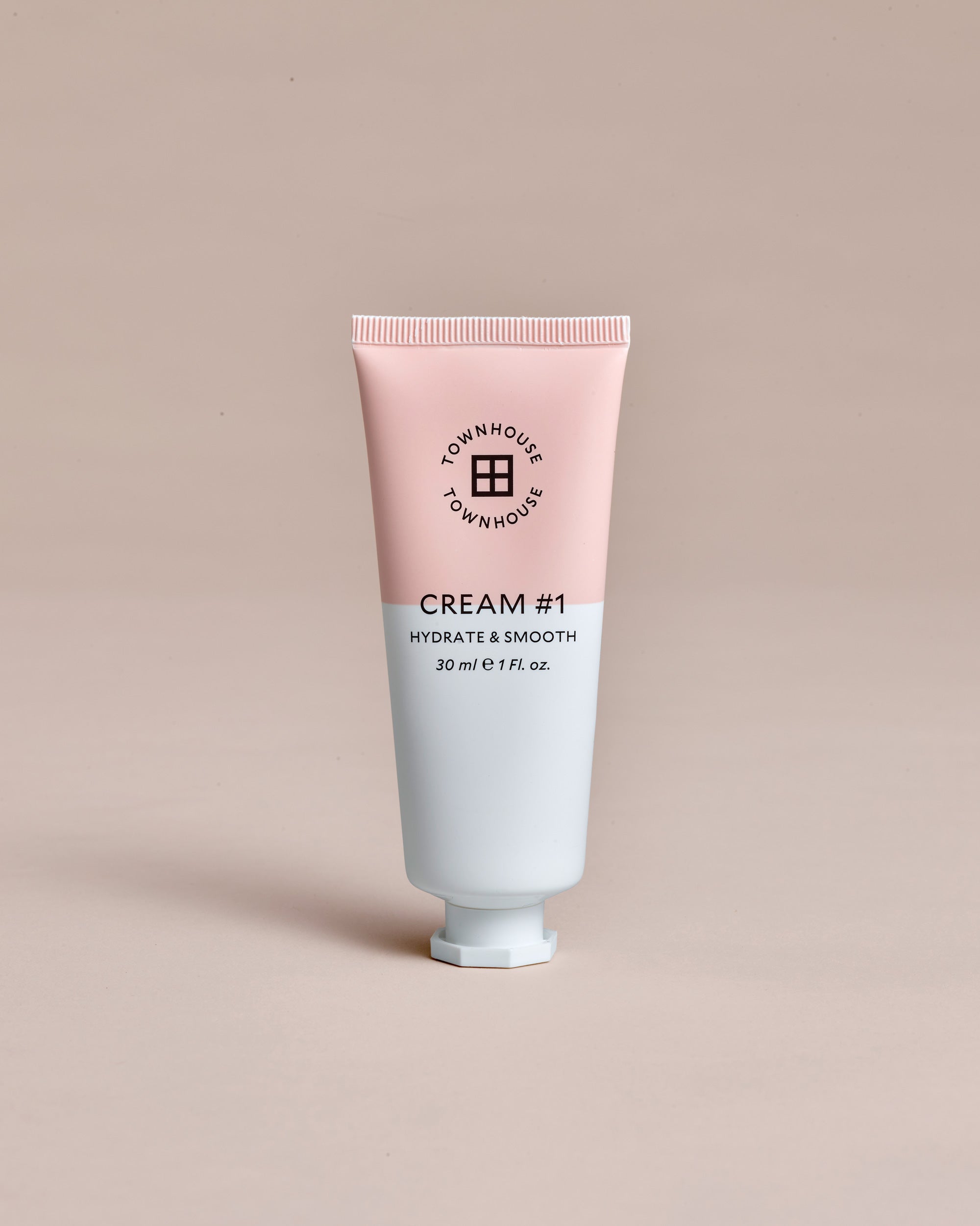 A 30ml tube of Townhouse Cream#1, featuring a pink and white design, is displayed upright against a beige background. This vegan moisturizer offers a coconut-scented cream formula that leaves your skin feeling refreshed and nourished.