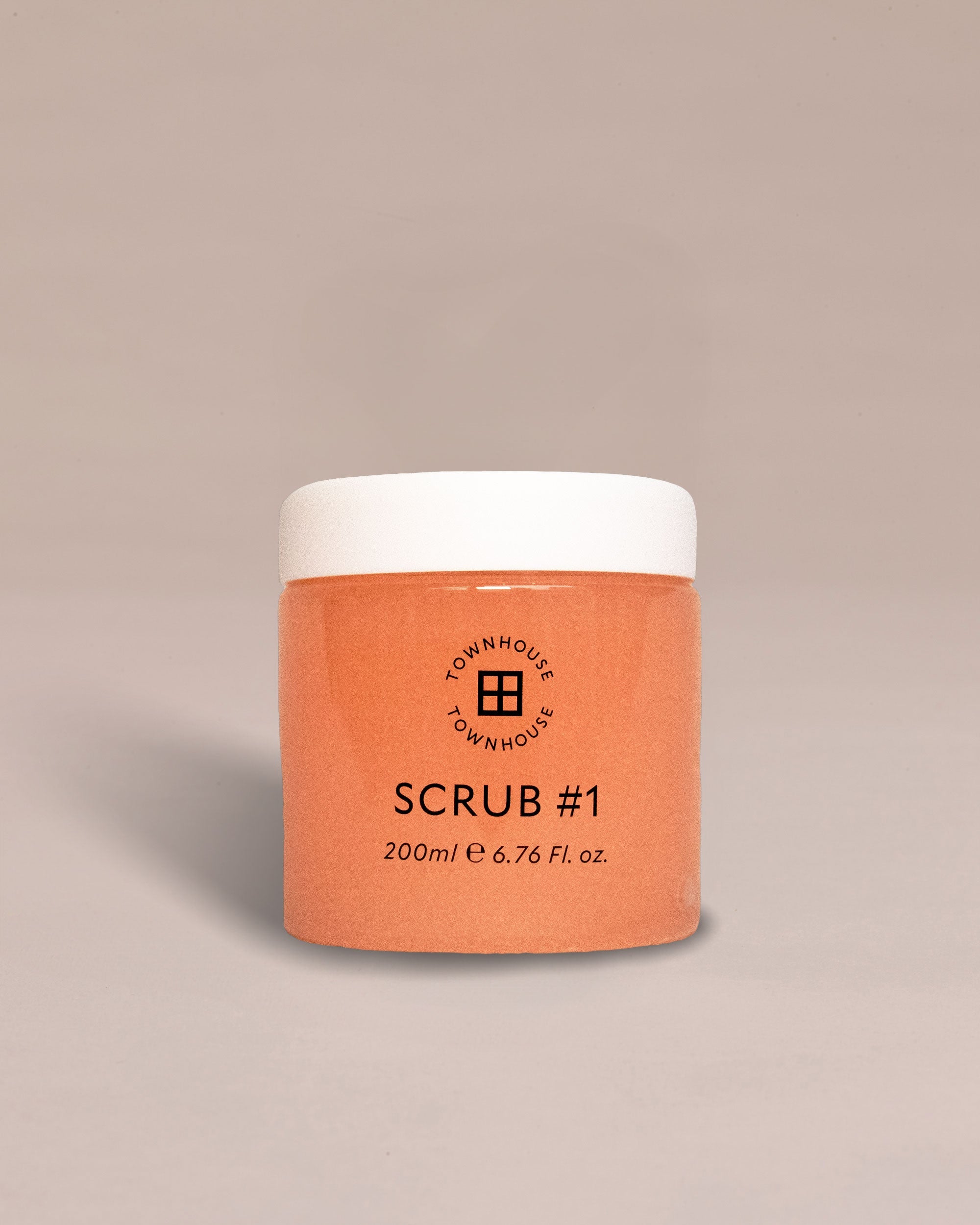 A peach-toned jar labeled "Townhouse Scrub #1 200ml," set against a plain beige backdrop, presents a coconut body scrub designed to gently polish the skin and reveal a radiant glow.
