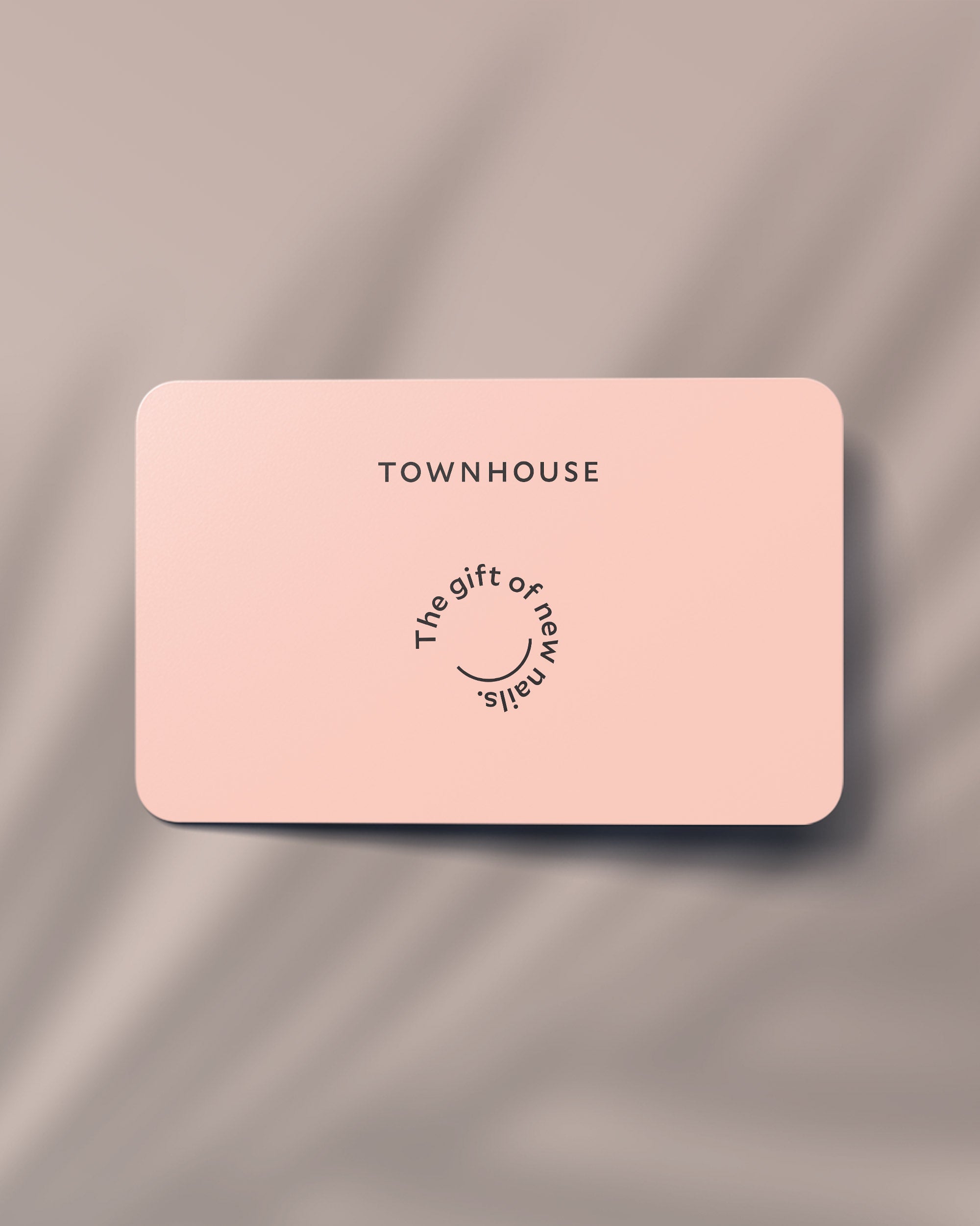 A pink rectangular card with rounded corners displays TOWNHOUSE at the top, with curved text reading The gift of new nails around a small smile illustration—making it the perfect £50 Townhouse Gift Card for nail treatments at your favorite salon. The card rests on a softly blurred beige background.